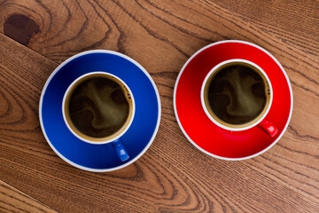 Two cups of hot coffee top view. Red and blue mugs with plates. Brown wooden surface on background.