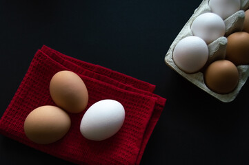 Several eggs on a red napkin and a cardboard container with eggs on the dark background.