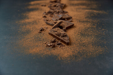 Dark chocolate stack, chips and cocoa powder on a dark background. Confectionery and food concept. Top view, copy space, selective focus.