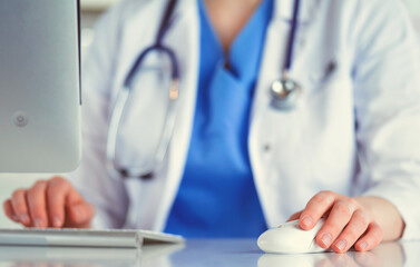 Young practitioner doctor working at the clinic reception desk, she is answering phone calls and scheduling appointments
