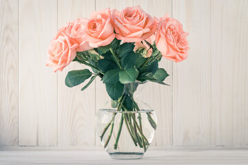 Bouquet of pink roses in a vase on a wooden board background. Still life in retro style. Vintage gift card, holiday concept decoration.