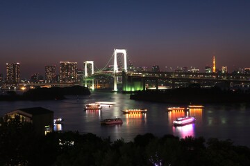 Tokyo, Japan - May 25, 2019: Illuminated Rainbow Bridge from Odaiba (お台場). Yakata bune (restaurant boats) are on the water.