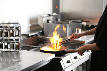 Female chef cooking meat with burning flame on stove in restaurant kitchen, closeup
