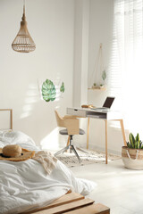 Stylish room interior with workplace and bed