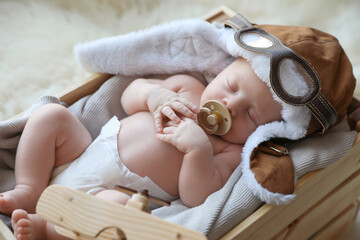 Cute newborn baby wearing aviator hat with toy sleeping in wooden crate