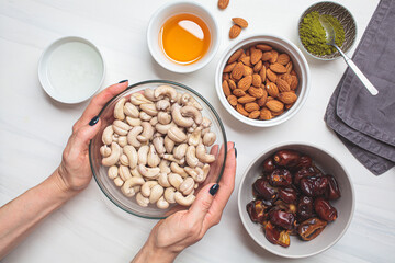 Ingredients in bowls for cooking raw vegan cake with nuts, dates and matcha tea, top view. Healthy vegan food concept.