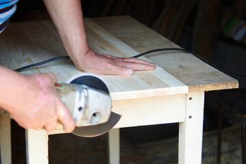 a worker using a sanding machine works with wood in a carpenter's workshop