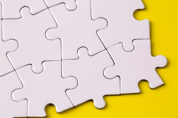 Fototapeta premium Missing jigsaw puzzle pieces. Business concept. Fragment of a folded white jigsaw puzzle and a pile of uncombed puzzle elements against