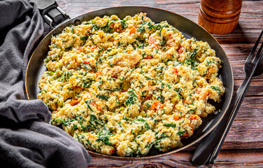 scrambled eggs with spinach and tomato in pan on wooden table background