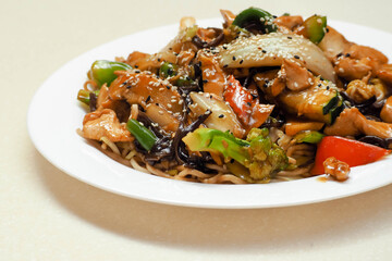 Asian cuisine  on a white plate are vegetables, sesame seeds, wok cooked in a pan and soba buckwheat noodles . spicy chicken and soba noodles