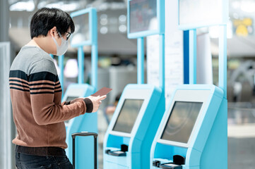 Asian man tourist wearing face mask using self check-in kiosk in airport terminal. Coronavirus...