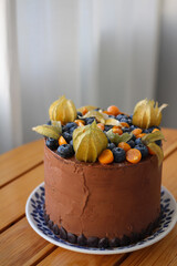 Homemade chocolate cake with rosebuds and blueberries, stands on a wooden table.