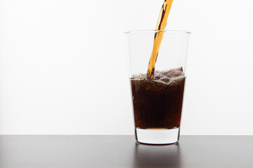 Cola drink pouring into a transparent glass on a wooden table on a white background