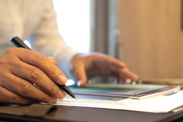 Document report and business busy concept: Businessman manager hands holding blue pen for reading and signing in paperwork or documentation files on computer modern corporate office background.