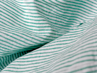 Fototapeta na wymiar Close view of crumpled bedding. Green striped cotton fabric. Cloth washing and laundry concept at home. Change of bed linen to clean.