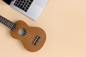 Laptop and ukulele on a beige background with place for text. Online education the play on a...
