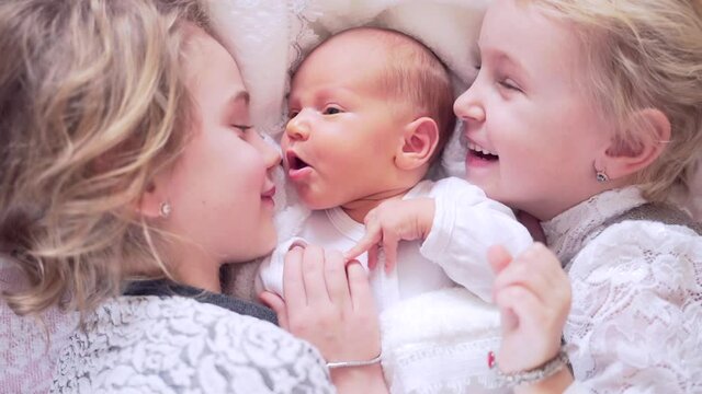 Three cute little children are lying on the bed. The sisters hug and kiss the newborn baby. Portrait of girls lying happy hugging close up. Happy and smiling together