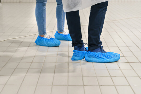 Close Up On Feet Of Unknown Man And Woman Wearing Overshoes - Blue Medical Shoe Covers For Protection On Floor In Hospital - Medical Antibacterial Plastic Disposable Pull On Slippers Hygiene Standard