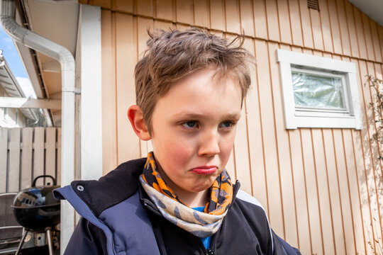 Outdoor portrait of a sad and angry boy in front of a small house.