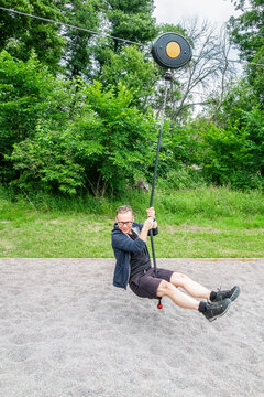 Fit male with glasses riding a zip-line at an outdoor playground at a public park.