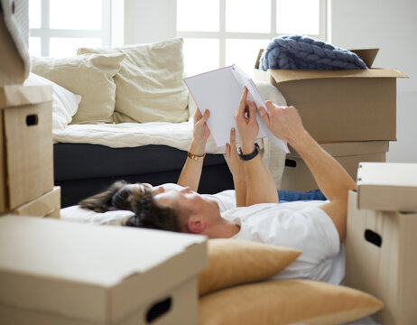 Cute couple unpacking cardboard boxes in their new home, lying on the floor and looking at a family album