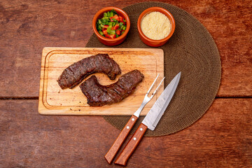 Delicious barbecue with pepperoni, seasoned on a wooden board on the table.Grilled steak with farofa and salad on a cutting board on the wooden table.
