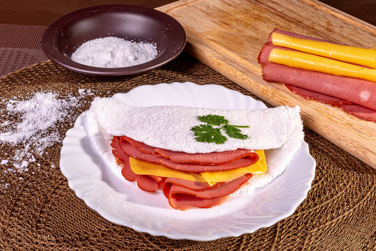 Tapioca beiju with ham, cheese and bologna on a plate on the table.