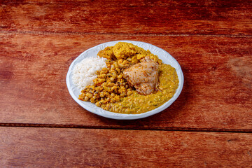Delicious Caruru. Traditional Afro-Brazilian dish made with okra and dried shrimp, accompanied by vatapa, beans, rice, chicken and farofa. On a wooden table.
