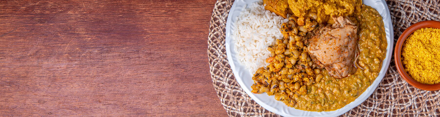 Delicious Caruru. Traditional Afro-Brazilian dish made with okra and dried shrimp, accompanied by vatapa, beans, rice, chicken and farofa. On a wooden table.