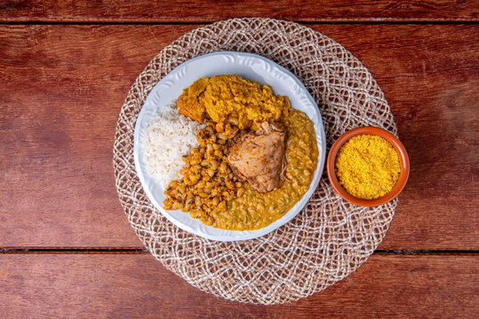Delicious Caruru. Traditional Afro-Brazilian dish made with okra and dried shrimp, accompanied by vatapa, beans, rice, chicken and farofa. On a wooden table.