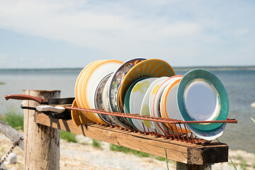 Tableware from different collections in the backyard at the seaside. Old drying rack full of washed various plates. Sunny summer day, blue sky, calm sea. Hippie commune life on tiny islet in Estonia.