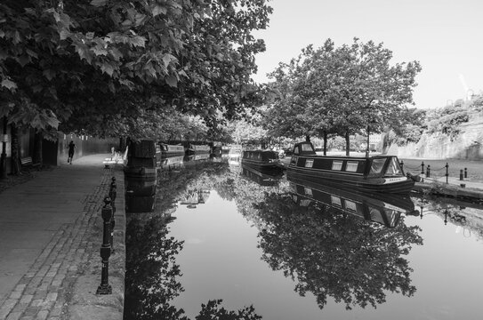 Black and white image of canal boats on the calm and reflective Bridgewater Canal at the former industrial area of Castlefield in Manchester.