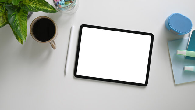 The top view image of a white blank screen computer tablet is putting on a comfortable working desk.