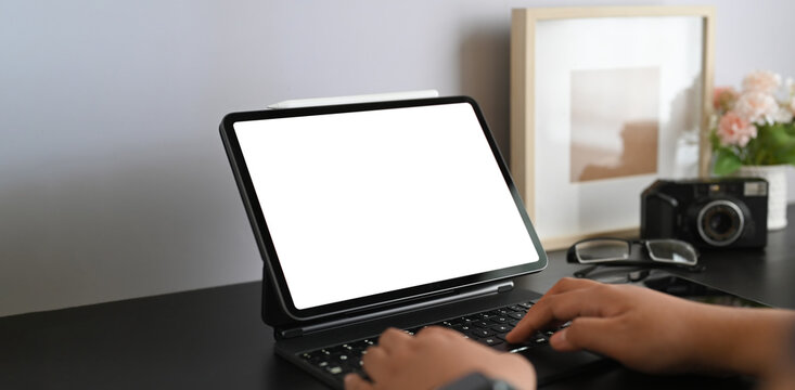 A cropped image of a woman is using a white blank screen computer tablet while sitting in the living room.