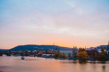 Fototapeta premium Dramatic sundown in the Vltava River with a boat passing by and a gradient of orange to pink colors reflecting from the sky into the water.