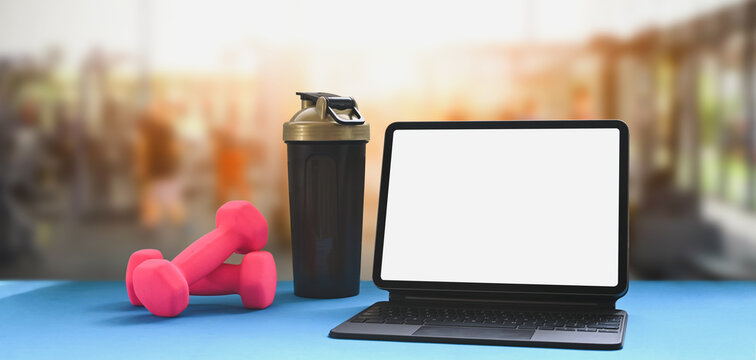 Computer tablet is putting on the table over a blurred gym as background.
