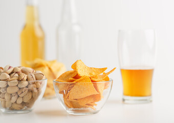Delicious snacks. Pistachios and nachos in glass bowls, bright ale in glass, empty bottle and full bottle drink