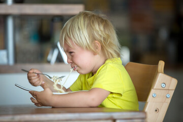 Cute blond boy, child eating spaghetti, crying with tantrum