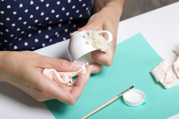 Roses with petals made of white polymer clay. A woman sticks them on a mug. Crafts from polymer...