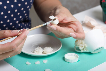 Roses with petals made of white polymer clay. A woman sticks them on a saucer. Crafts from polymer clay.