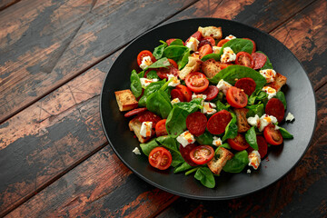 Chorizo Tomato salad with spinach, feta cheese and croutons on black plate. healthy summer food