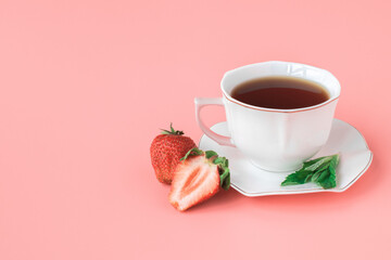 Cup of tea on a white saucer with mint leaves and ripe strawberries. pink background. copyspace.