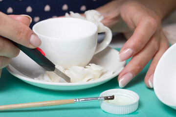 Roses with petals made of white polymer clay. A woman sticks them on a saucer. Corrects with a clerical knife. Crafts from polymer clay.