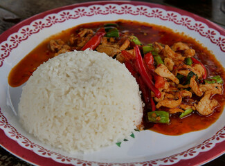 stir-fried pork with thai chili paste and rice on the white dish on wooden table.Thai food