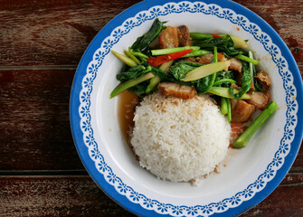 Crispy Pork Belly Stir Fry With Chinese Kale With rice in plate on wood table background.