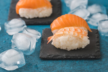 Closeup of Nigiri sushi on slate with ice cubes on blue background