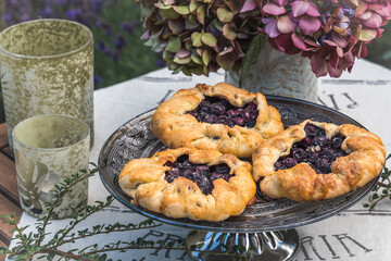 Homemade blueberry galettes on a table with hydrangea flowers and light green glasses for candles. Closeup.