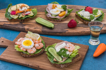 Variety of danish open sandwiches on wooden boards and blue background, decorated with different...