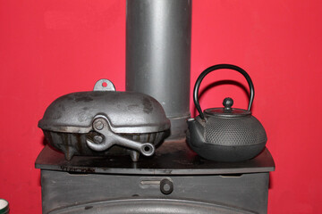 Ready for a power cut, kettle and potato baker on top of a log burner, with red painted wall behind - 362379352