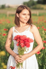 A girl in white dress holding a bouquet of poppies in a poppy field